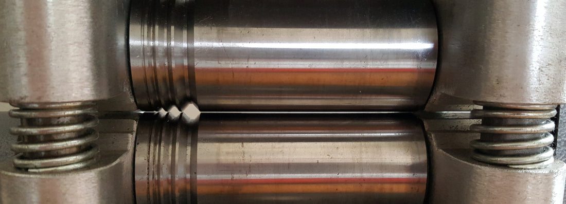 Detail of a rolling mill, a tool used in metalwork. At the centre are two horizontal cylinders made of polished steel.